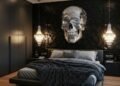 A moody bedroom with a large ornate silver skull sculpture mounted on a black 3D-paneled wall above a leather bed and crystal pendants.