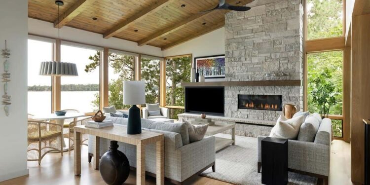 Living room with lake-view windows, stone fireplace, and a pleated pendant over the round table