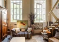 Historic London apartment with tall windows, aged parquet flooring, an antique wooden armoire, striped sofa, modern artwork, and a contemporary metal staircase.